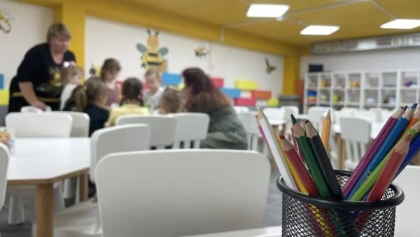 Діти з вихователями за столом у групі дитсадка, на передньому плані кольорові олівці