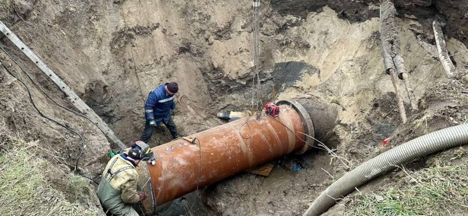 Робітники опускають великий колектор у котлован за допомогою крана