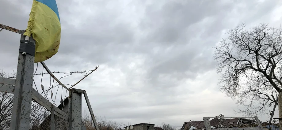 Український прапор на іржавій брамі з колючим дротом біля зруйнованих будівель