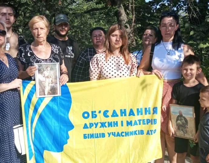 Дружини й матері захисників з дітьми тримають банер об’єднання та портрети бійців