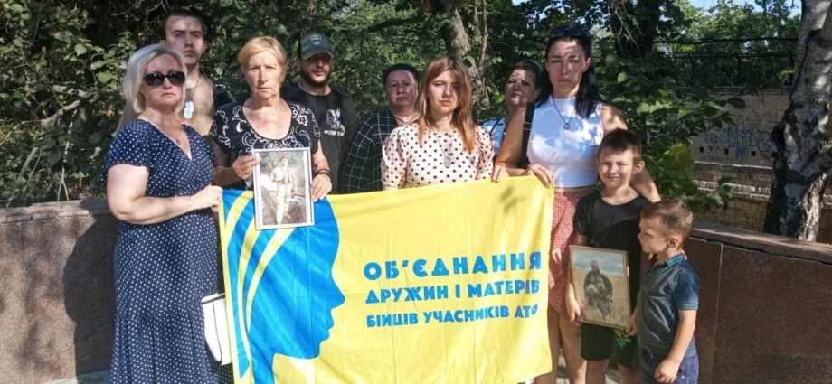 Дружини й матері захисників з дітьми тримають банер об’єднання та портрети бійців