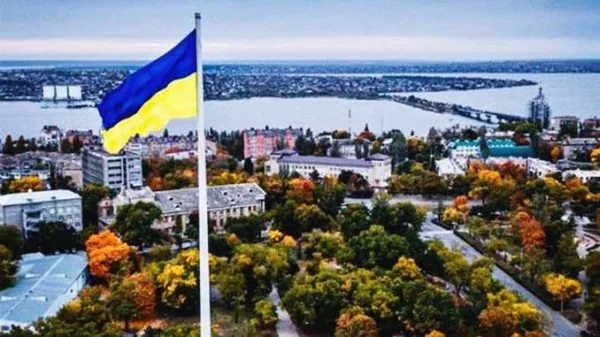 Український прапор на флагштоку над осіннім містом біля річки з мостом
