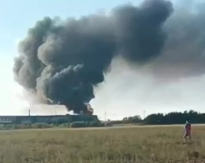 Густий чорний дим над довгою будівлею в полі, людина йде полем