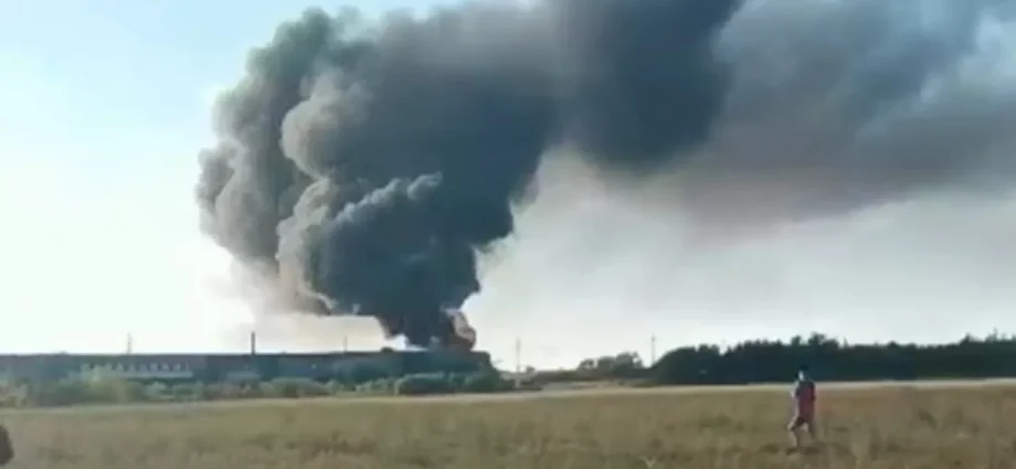 Густий чорний дим над довгою будівлею в полі, людина йде полем