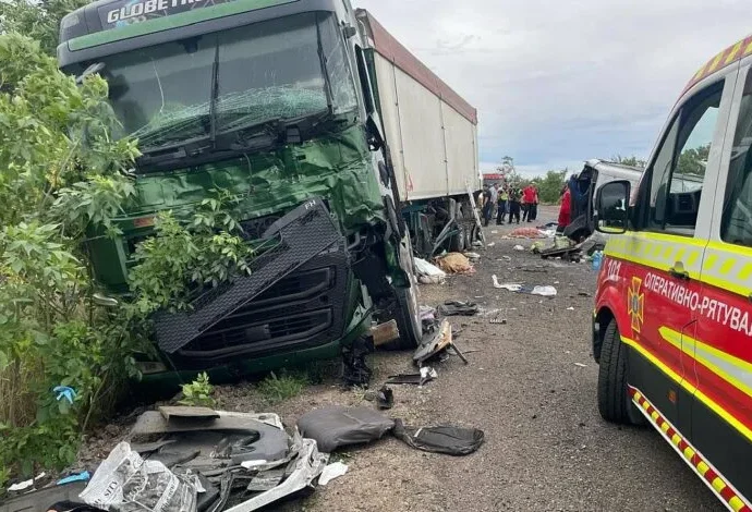Пошкоджена зелена вантажівка біля кущів і рятувальний автомобіль на узбіччі