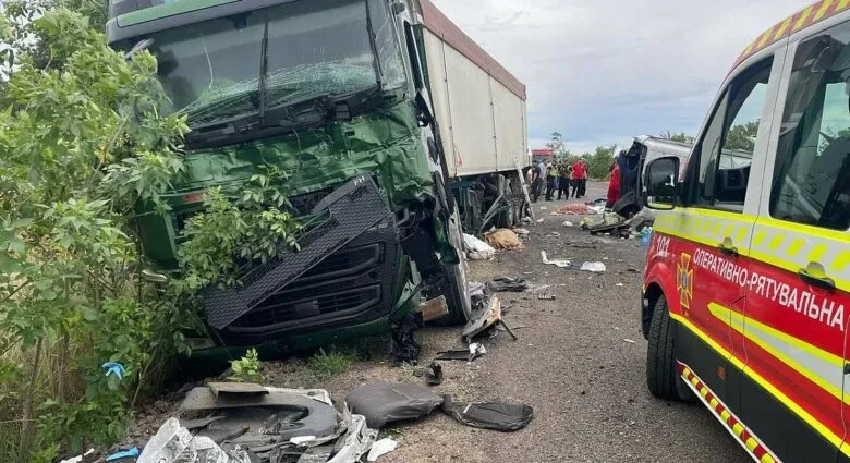 Пошкоджена зелена вантажівка біля кущів і рятувальний автомобіль на узбіччі