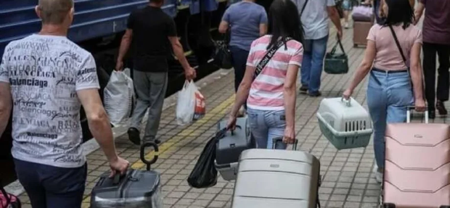 Люди з валізами йдуть пероном уздовж синього поїзда