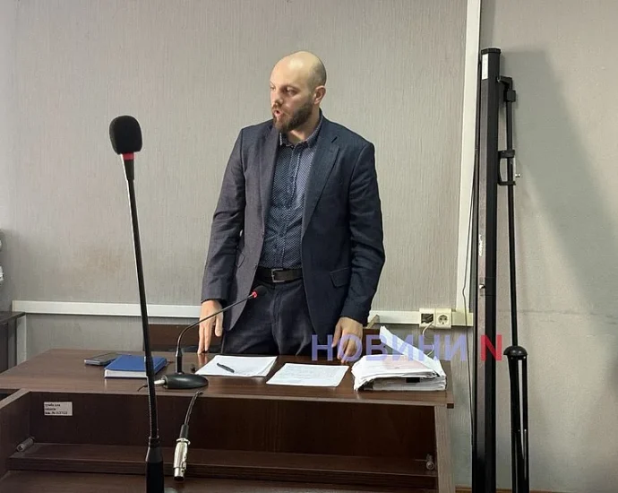 Чоловік у костюмі стоїть за судовою кафедрою з мікрофоном