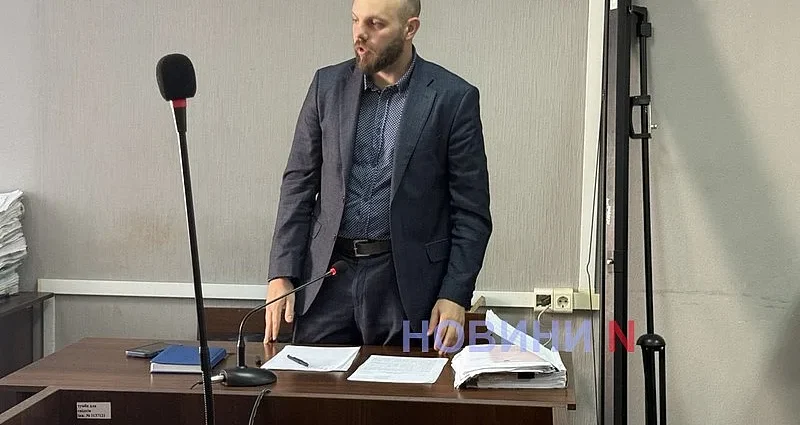 Чоловік у костюмі стоїть за судовою кафедрою з мікрофоном