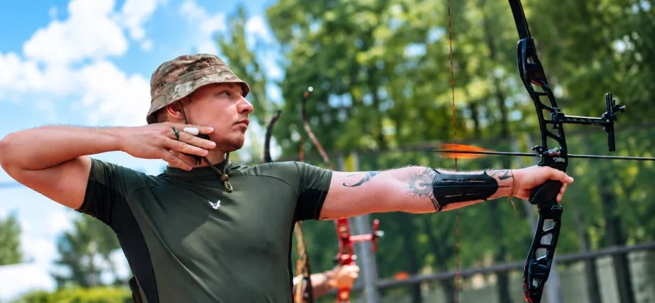 Чоловік у камуфляжній формі натягує тятиву лука на відкритому повітрі